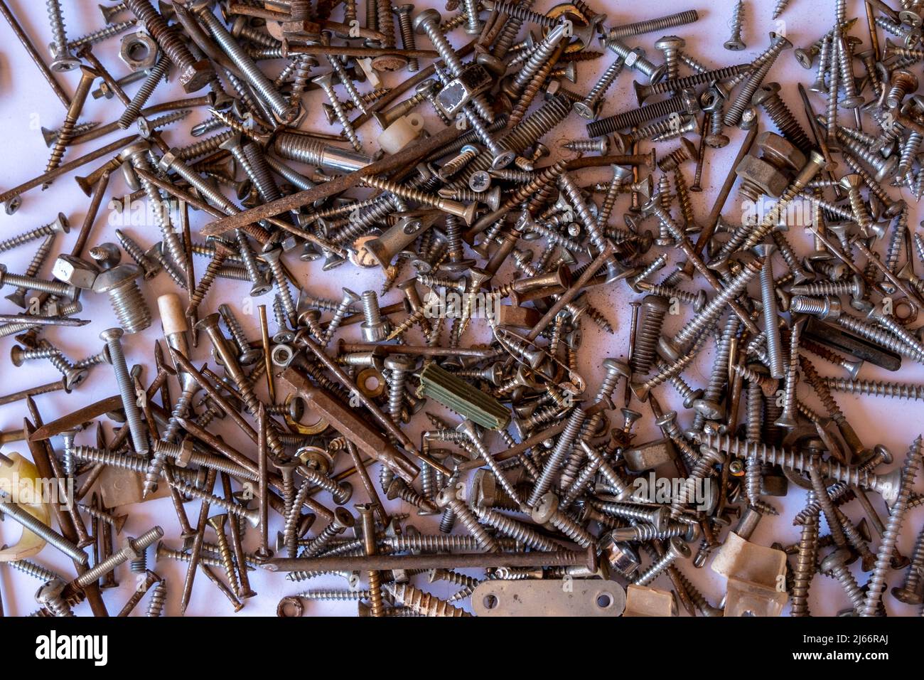 Mucchio di chiodi arrugginiti e piccoli dadi di ferramenta, mucchio di chiodi ossidati e rivetti sparsi sullo sfondo bianco, vista dall'alto Foto Stock