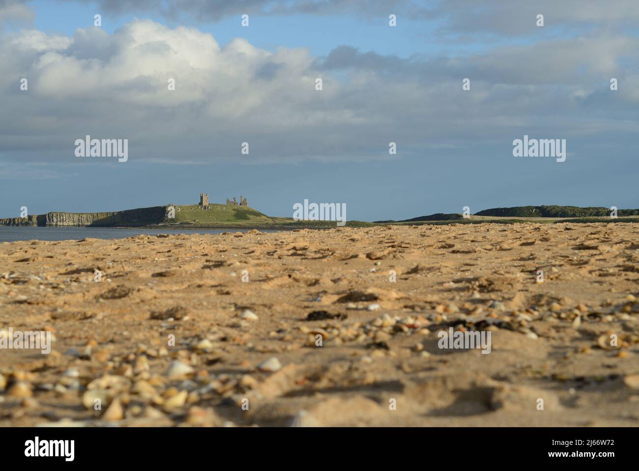 Paesaggio che mostra un lontano castello di Dunstanburgh sul suo affioramento scogliera visto dal livello della spiaggia vicino Embleton Foto Stock
