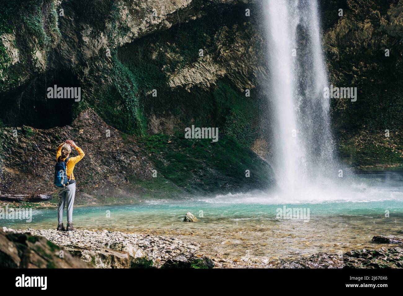 Donna escursionista guardando in alto in cima alla cascata nascosta Foto Stock