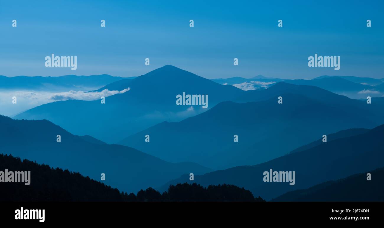 La silhouette delle montagne nella luce del mattino. Vista panoramica della catena montuosa coperta da foresta con cielo blu. Foto Stock