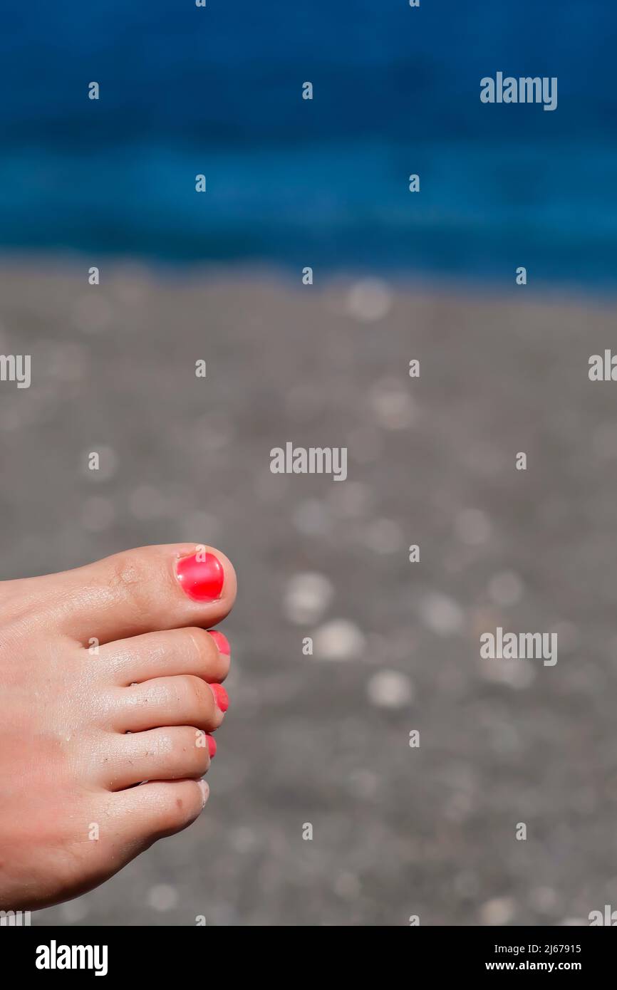 Primo piano vista di un piede femminile con vernice rossa unghie rilassante sulla spiaggia Foto Stock
