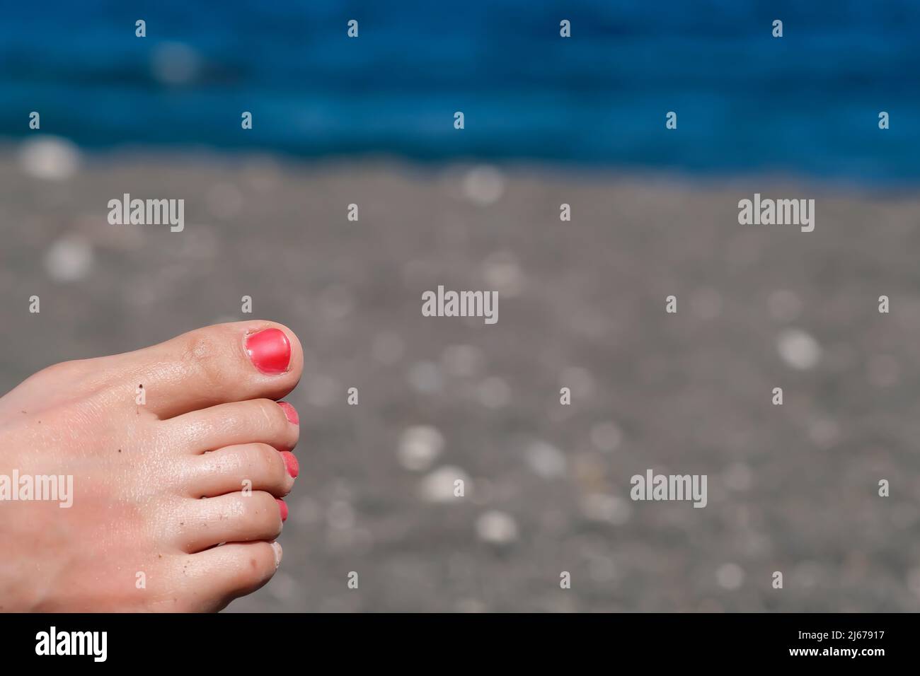 Primo piano vista di un piede femminile con vernice rossa unghie rilassante sulla spiaggia Foto Stock