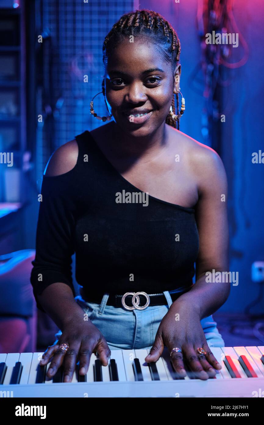 Verticale medio ritratto della giovane donna nera con tastiera digitale in studio di registrazione sorridente alla fotocamera Foto Stock