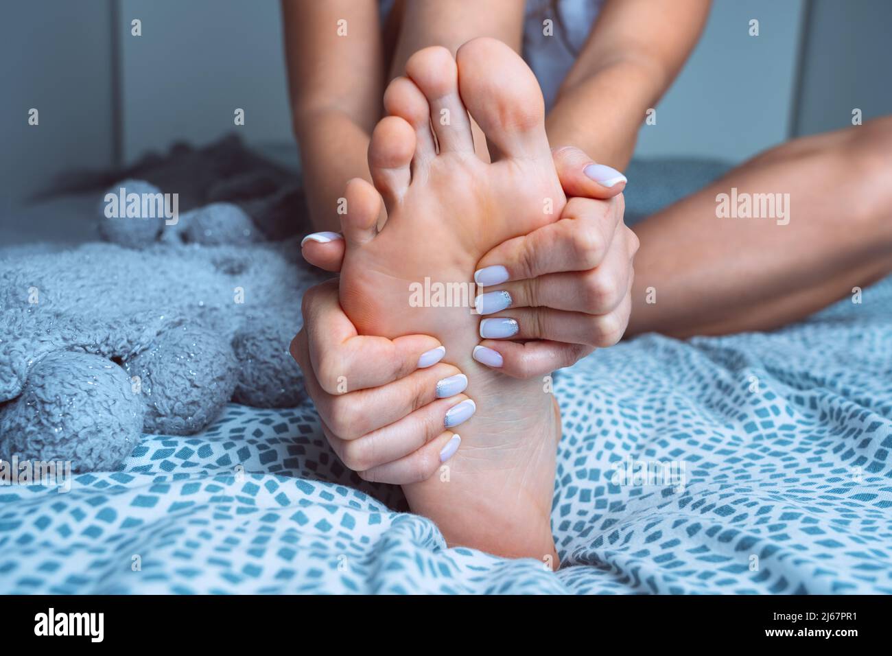 Donna che massaggiava piede stanco doloroso a letto. Dolore ai piedi crampi alle gambe, dolore alle gambe o spasmo muscolare Foto Stock