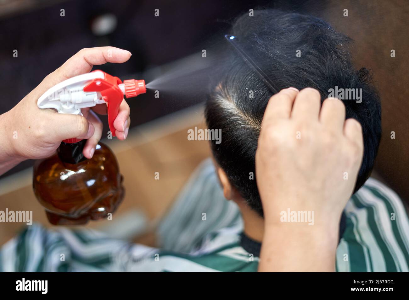 Le mani di un barbiere che utilizza un dispenser di acqua per bagnare i capelli del cliente Foto Stock