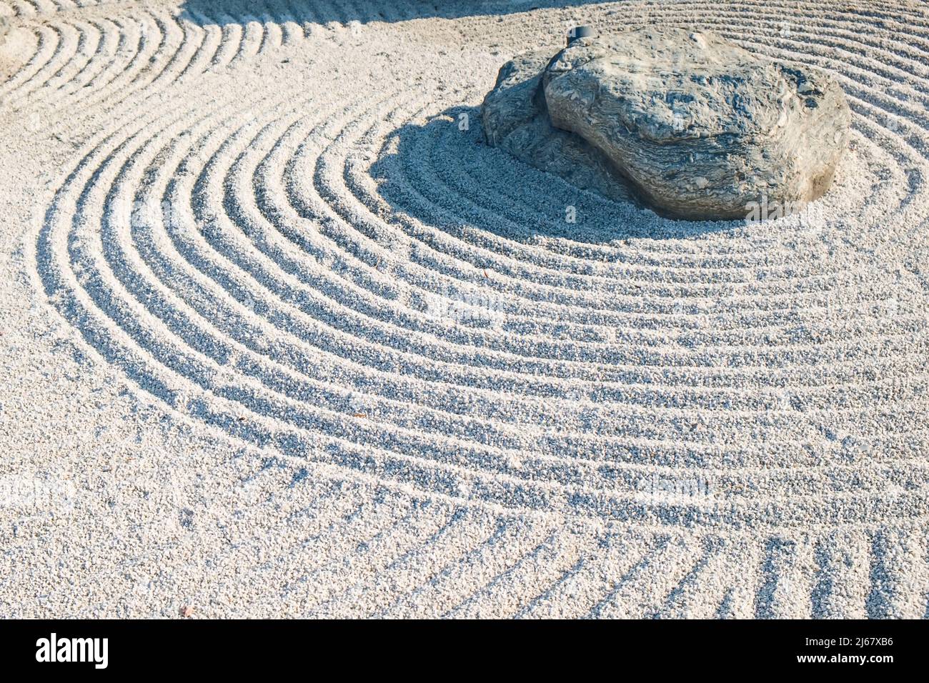 Dettagli tradizionali del Giardino Zen Giapponese classico. Pietra vulcanica circondata linee concentriche rastrellate su ghiaia.file simboliche in Ghiel Stones Garden Foto Stock