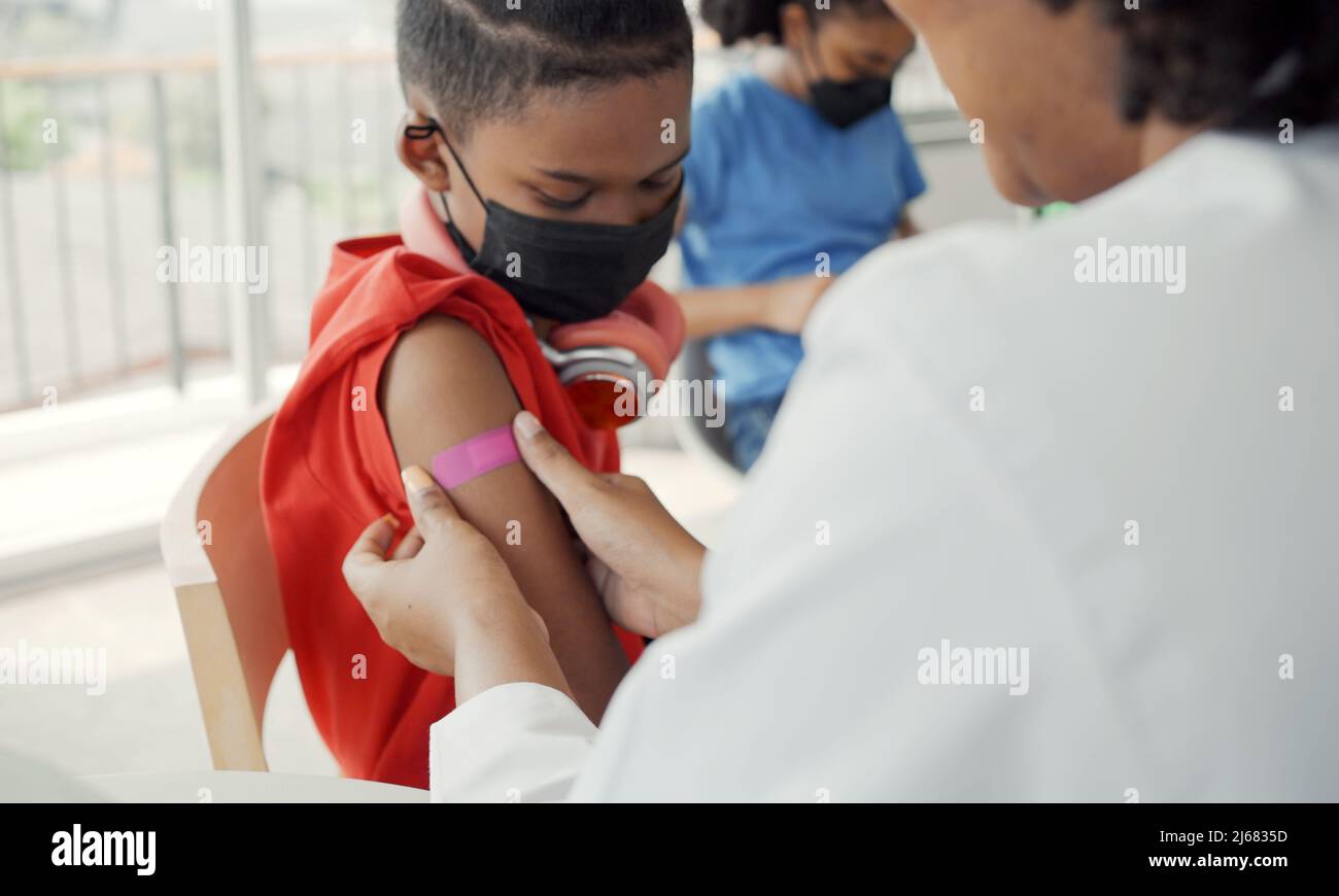 Il medico afroamericano sta applicando il gesso alla spalla di un bambino dopo essere stato vaccinato. Maniche di apertura per vaccinare contro l'influenza o l'epidemia in guarire Foto Stock