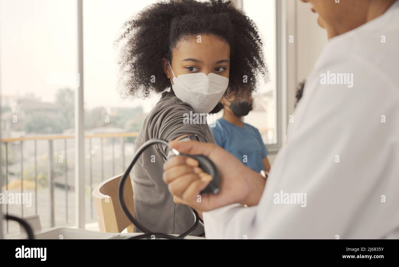 Il medico afroamericano sta misurando la pressione sanguigna e controllando il paziente del bambino del polso. Foto Stock