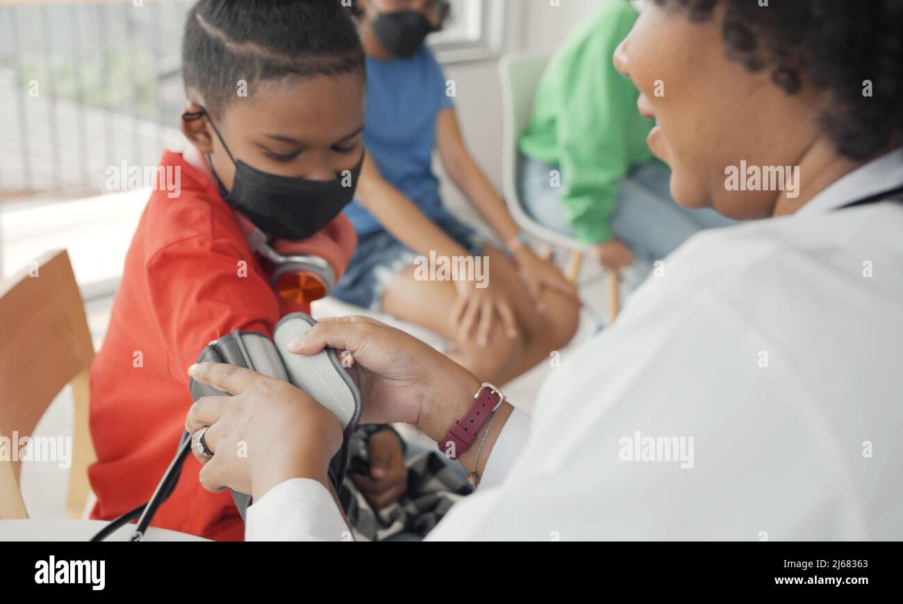Il medico afroamericano sta misurando la pressione sanguigna e controllando il paziente del bambino del polso. Foto Stock