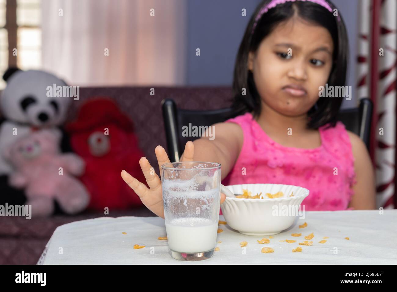 Fuoco selettivo su un bambino indiano della ragazza con pasto incompleto dei fiocchi di mais e del latte che mostra dissimile Foto Stock