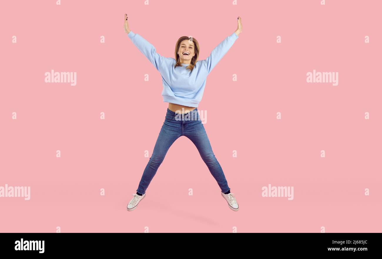Felice gioiosa giovane donna eccitata in abiti casual che saltano su sfondo rosa studio Foto Stock