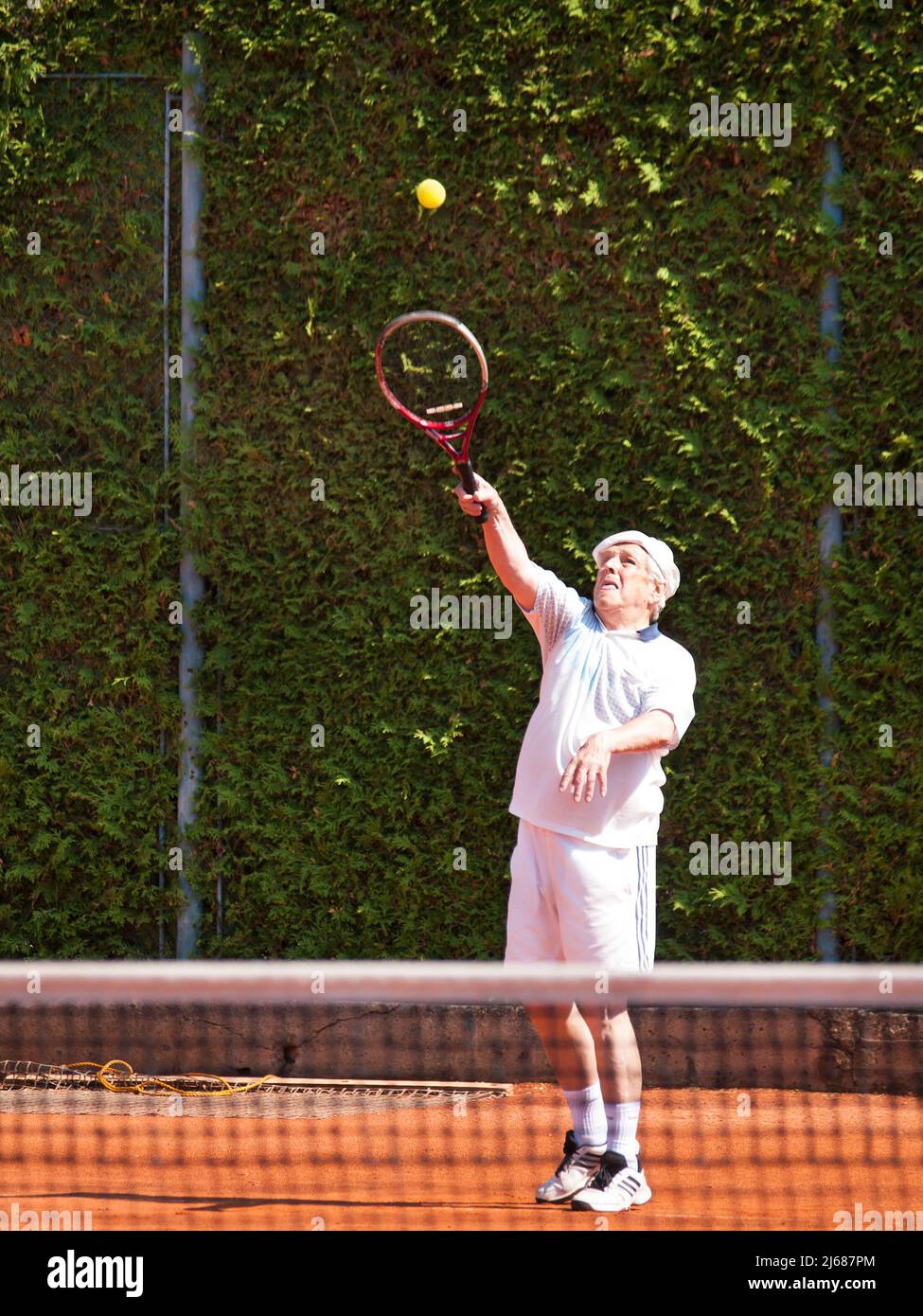 Corpo completo di uomini anziani in procinto di servire sul campo da tennis all'aperto. Foto Stock