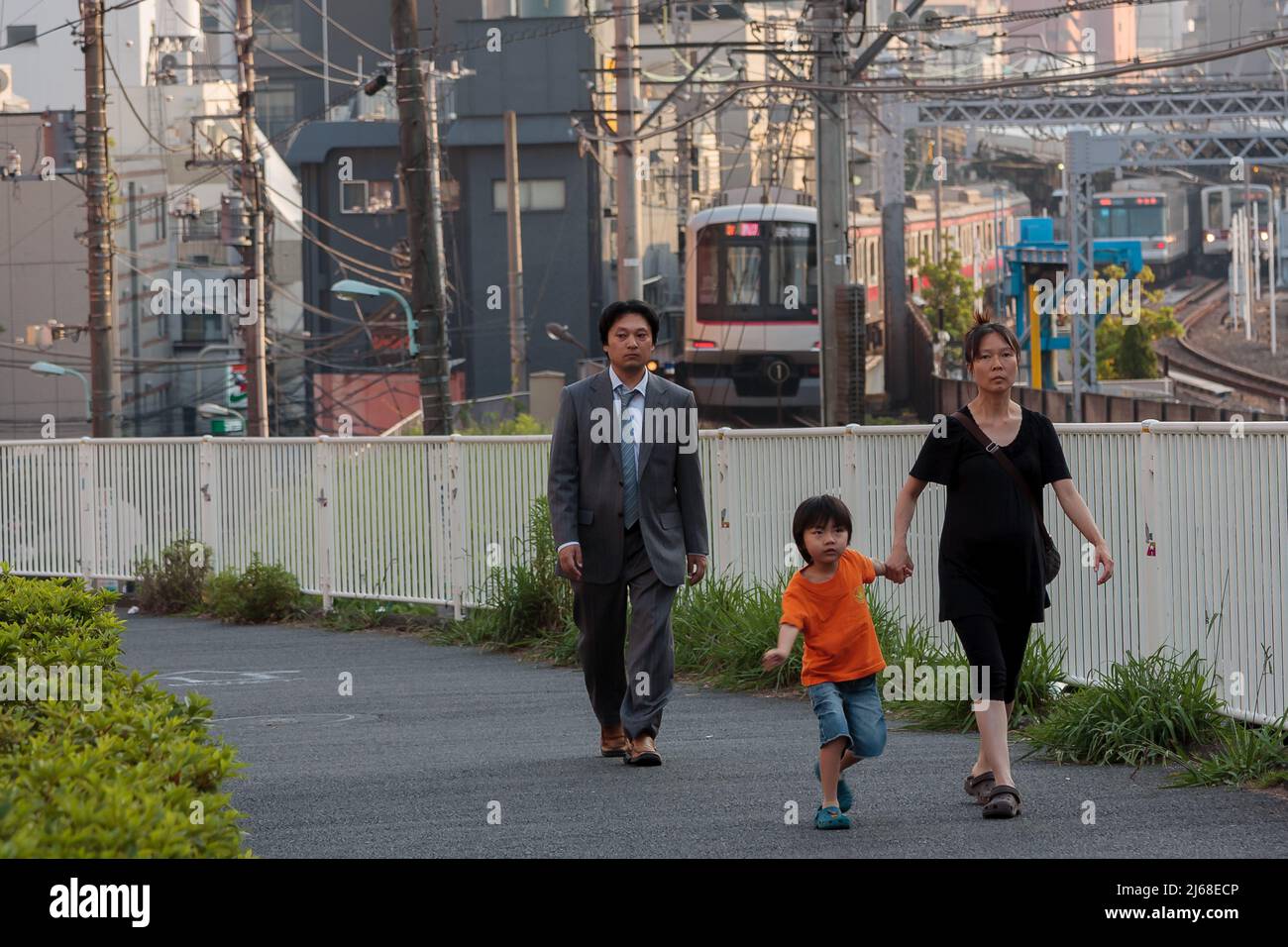 Una donna con un ragazzo giovane e un giovane lavoratore di ufficio o salarista cammina vicino ai binari dei treni a Nakameguro, Tokyo, Giappone. Foto Stock