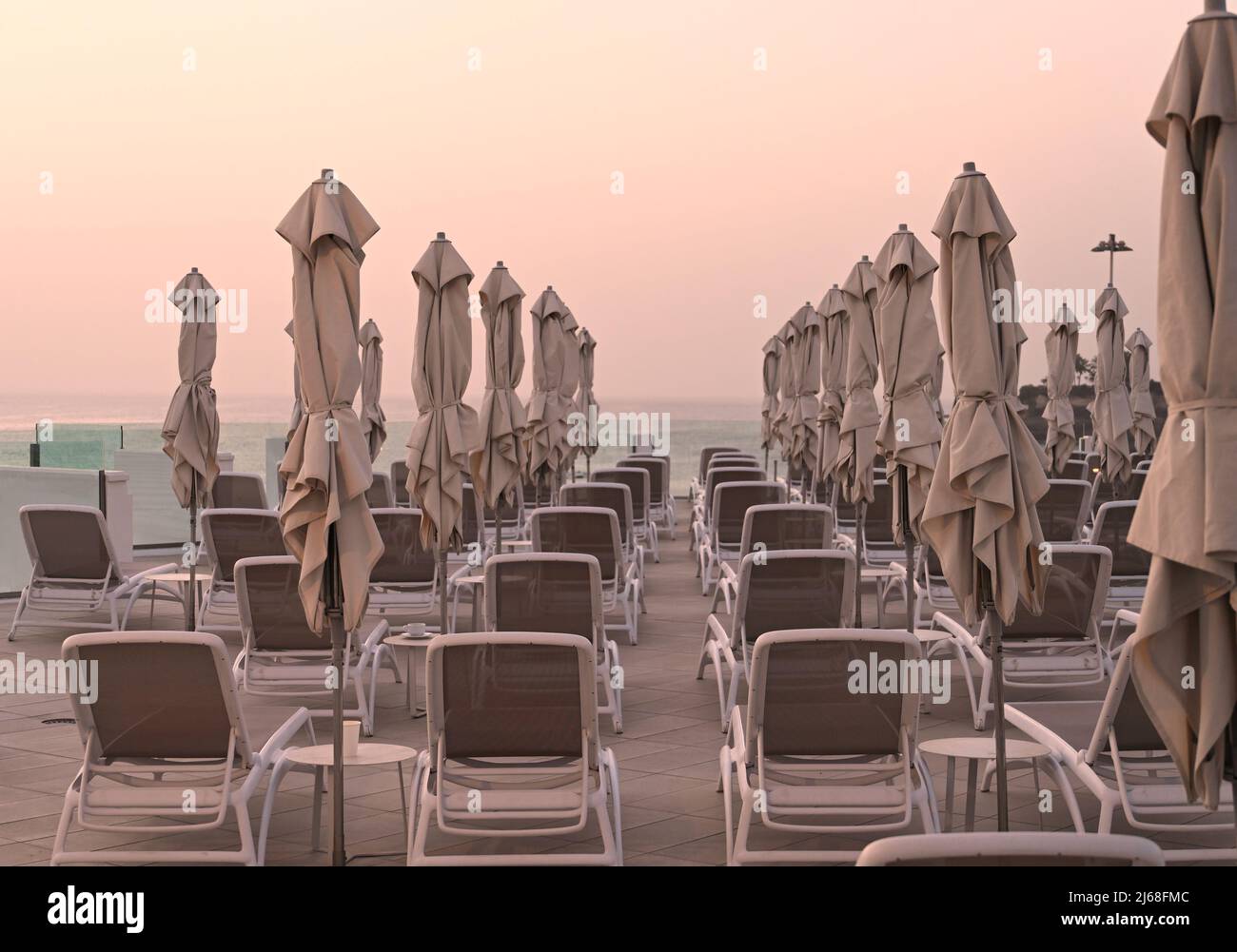 Una vista da dietro file di lettini con ombrelloni chiusi che si affacciano sull'Oceano Atlantico, destinazione di vacanza Tenerife, Costa Adeje, Spagna Foto Stock