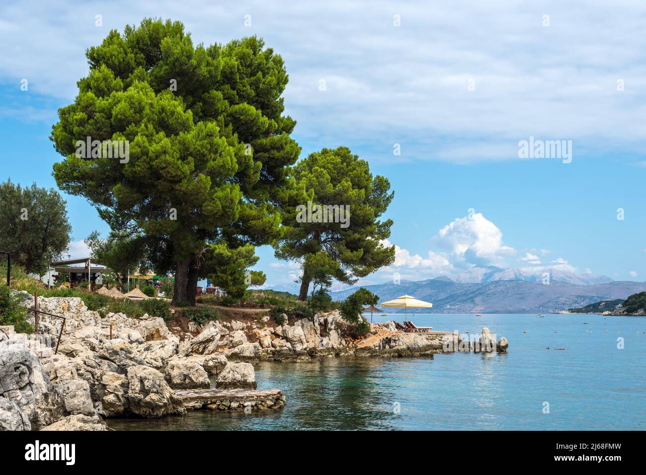 Ksamil, Albania - 9 settembre 2021: Mare con ombrelloni sulla spiaggia e un albero su una costa rocciosa a Ksamil, Albania. Destinazioni bellissime. T Foto Stock