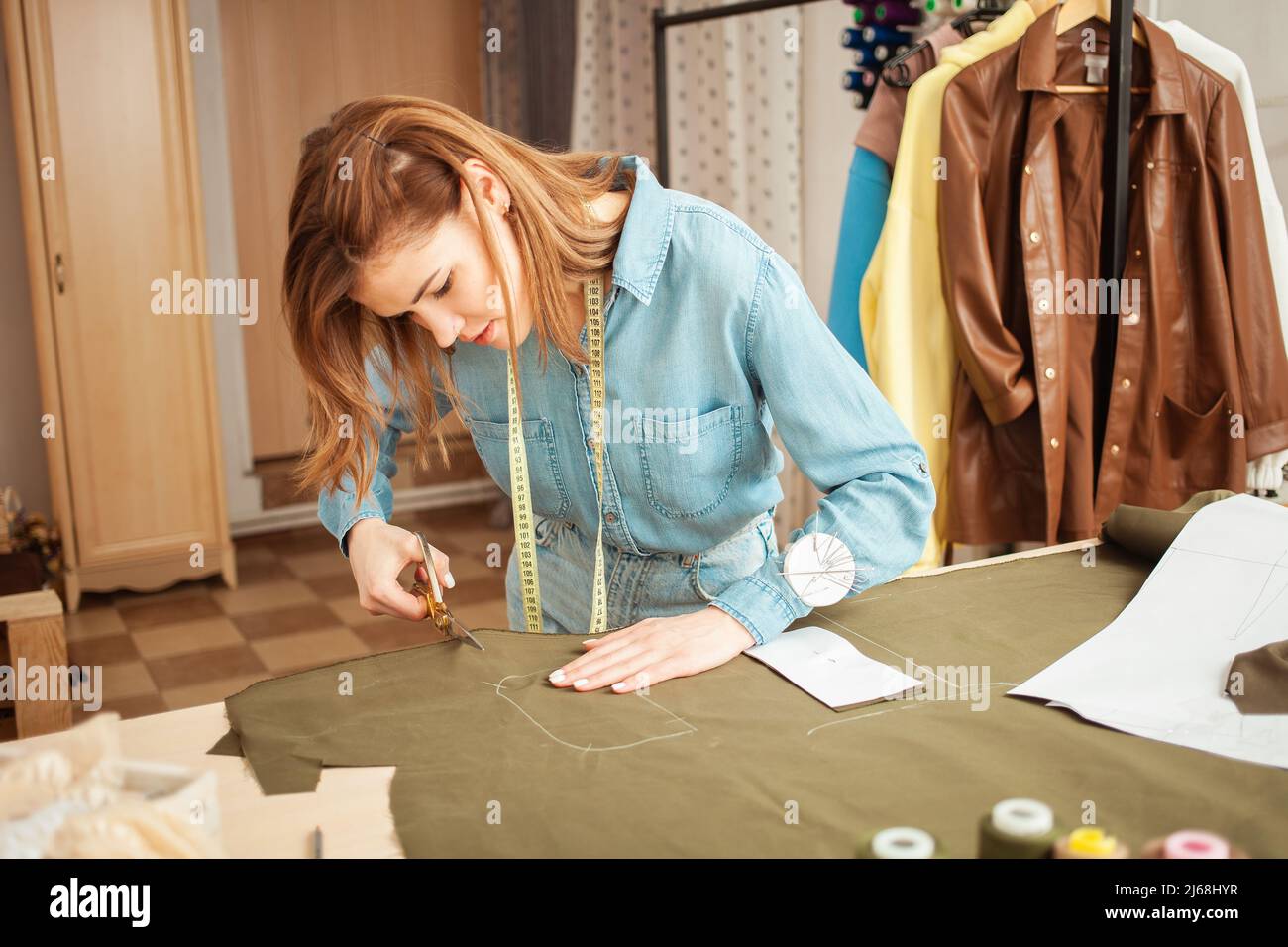 Seamstress ritagliato da dettagli di tessuto di futuri abiti, modello. Elegante studio di cucito, piccola impresa, al chiuso. Forbici Foto Stock