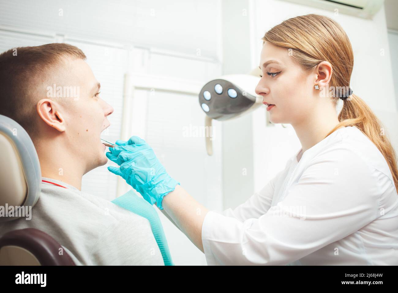 Medico dentista femminile europeo tratta il paziente, esamina la bocca e i denti. Servizio professionale, cordiale, sorridente, felice e soddisfatto, calmo Foto Stock