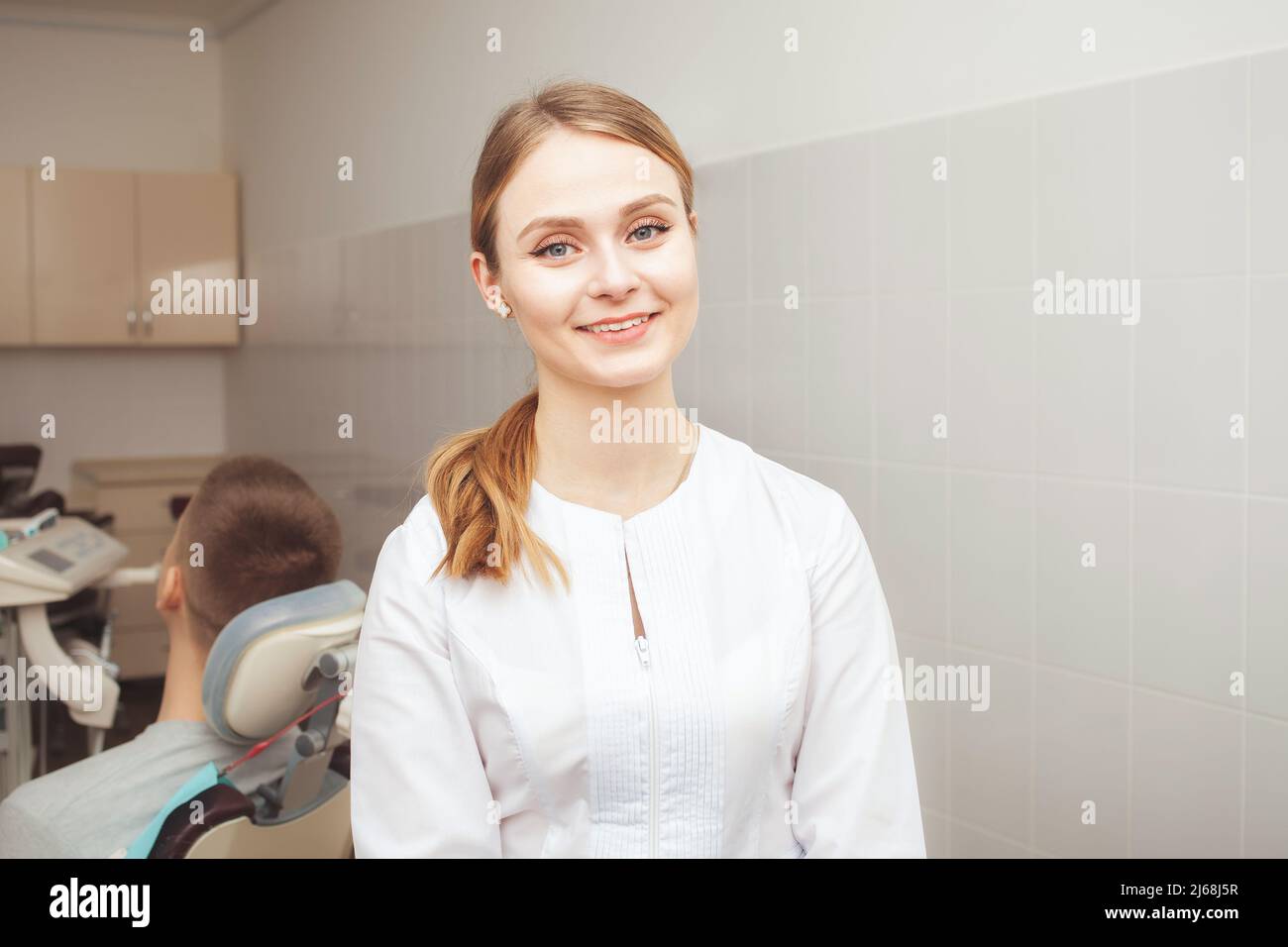 Ritratto di bella donna medico, dentista in clinica contro sfondo di paziente in ufficio. Sorridente, felice, disposto a se stessa. Foto Stock