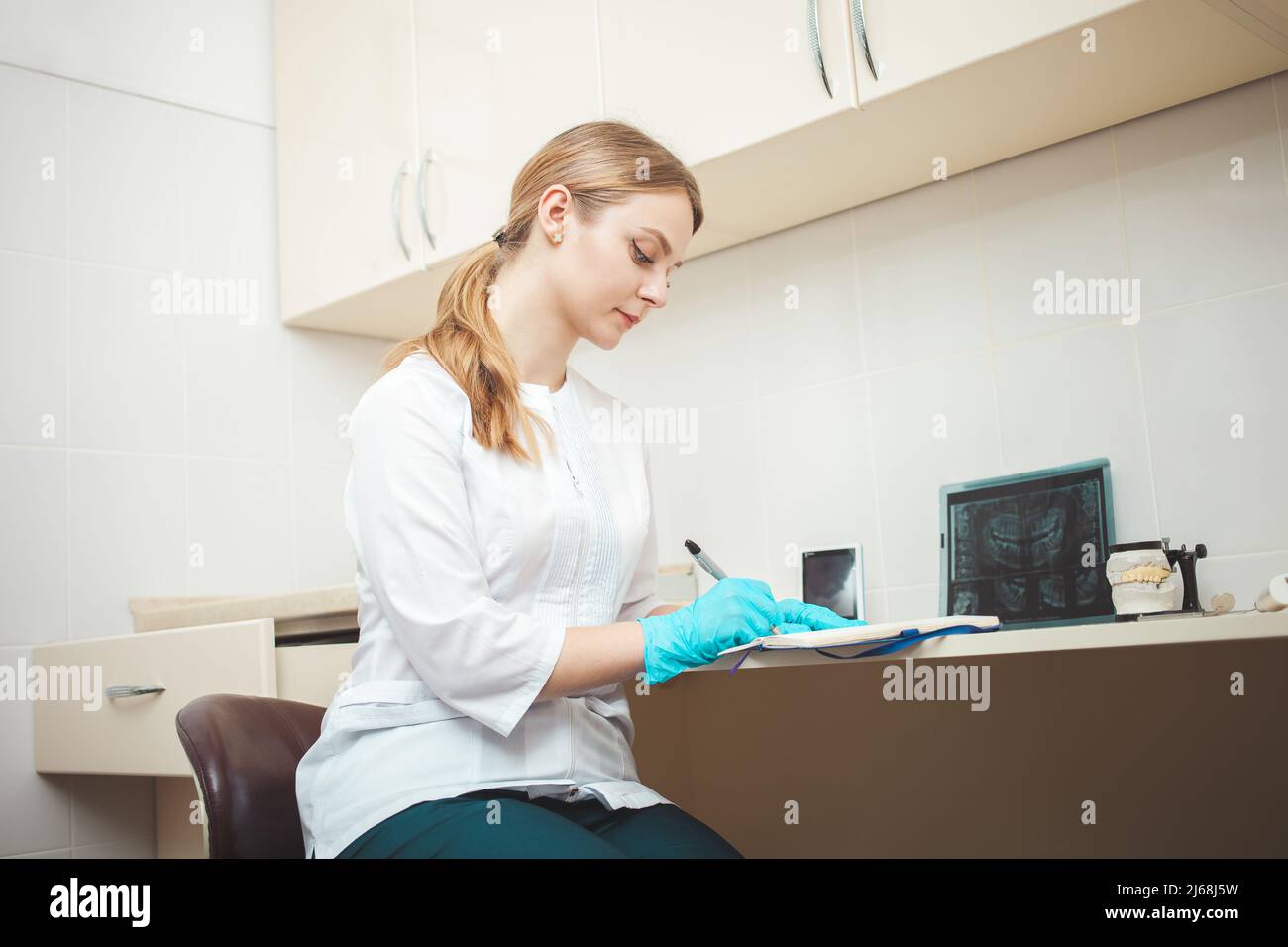 bella donna dentista in ufficio, in clinica, al coperto. Ritratto, sorridente e felice. Medico amichevole. Effettua registrazioni con penna Foto Stock