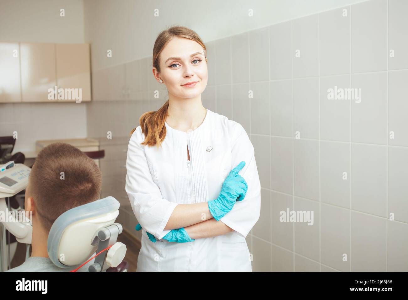 Ritratto di bella donna medico, dentista in clinica contro sfondo di paziente in ufficio. Sorridente, felice, disposto a se stessa. Professionale Foto Stock