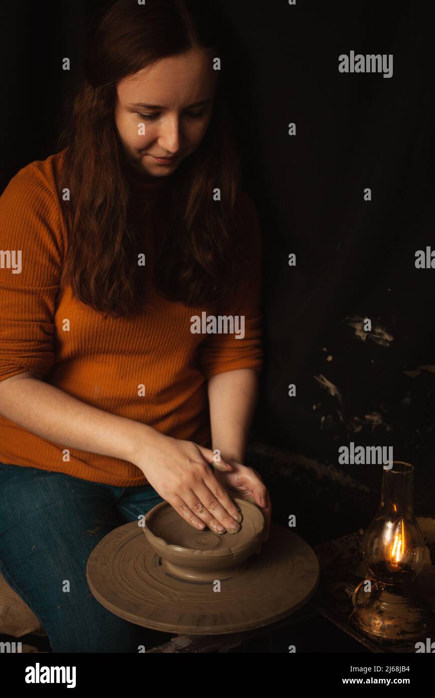 donna fa piatto di argilla in laboratorio di ceramica, sorrisi, felice, bello, sfondo, atmosfera autentica, stile di vita. lampada gialla Foto Stock