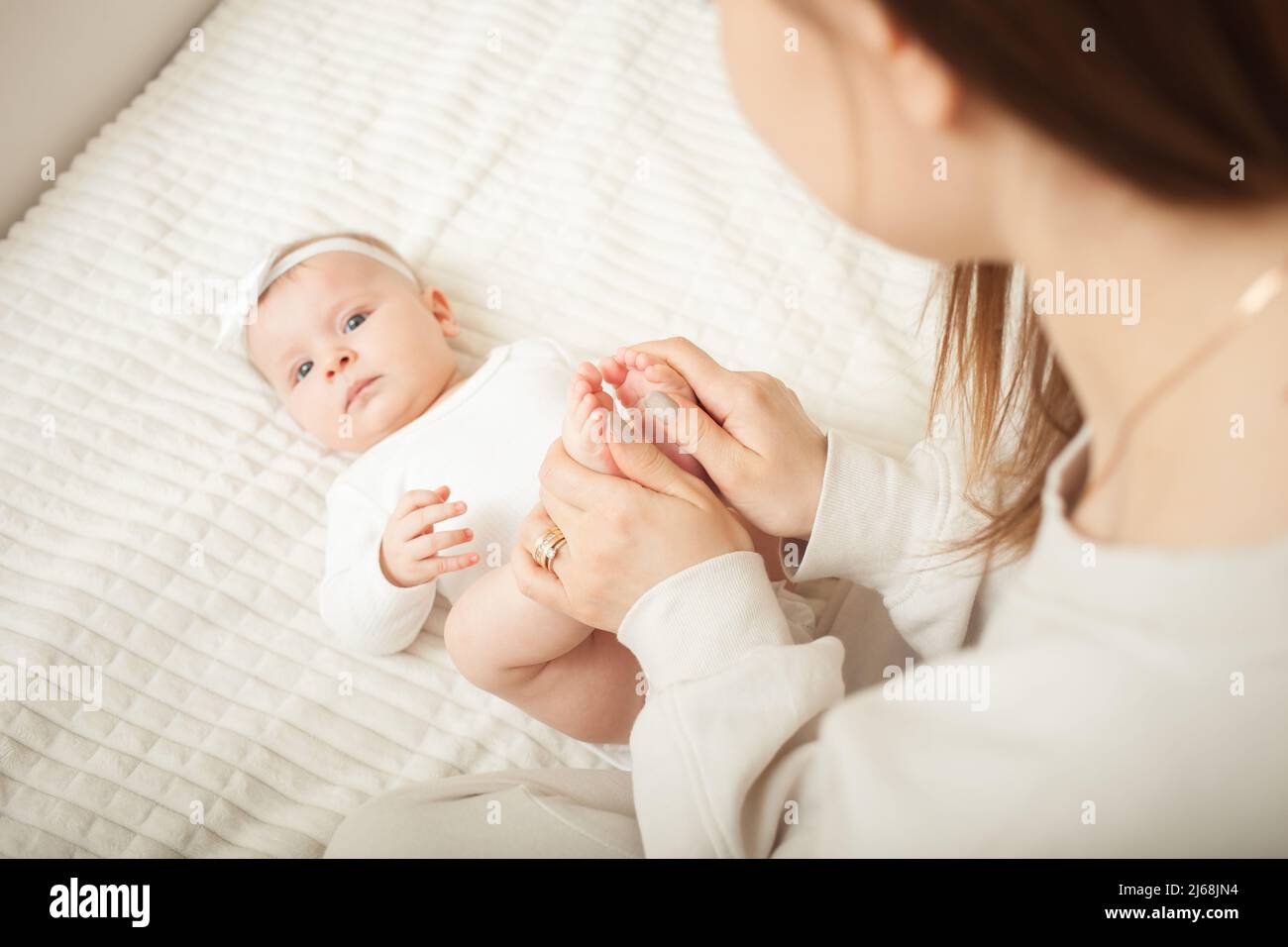 la madre massaggia la bambina, neonato. si trova a letto in camera da letto, a casa. Gambe, dita. Foto Stock