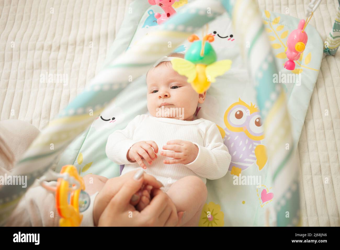 il bambino si trova sul letto, giocattoli appesi, materassino del bambino, ragazza neonata. sviluppante, guardando i giocattoli soddisfatti Foto Stock