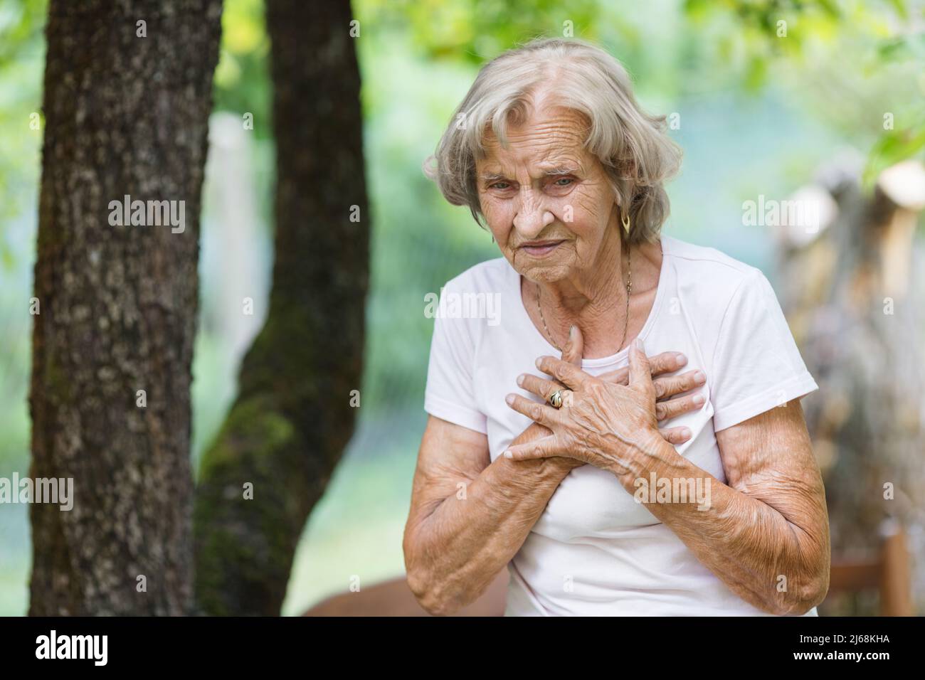 Donna anziana all'aperto con dolore al cuore che tiene il suo petto Foto Stock