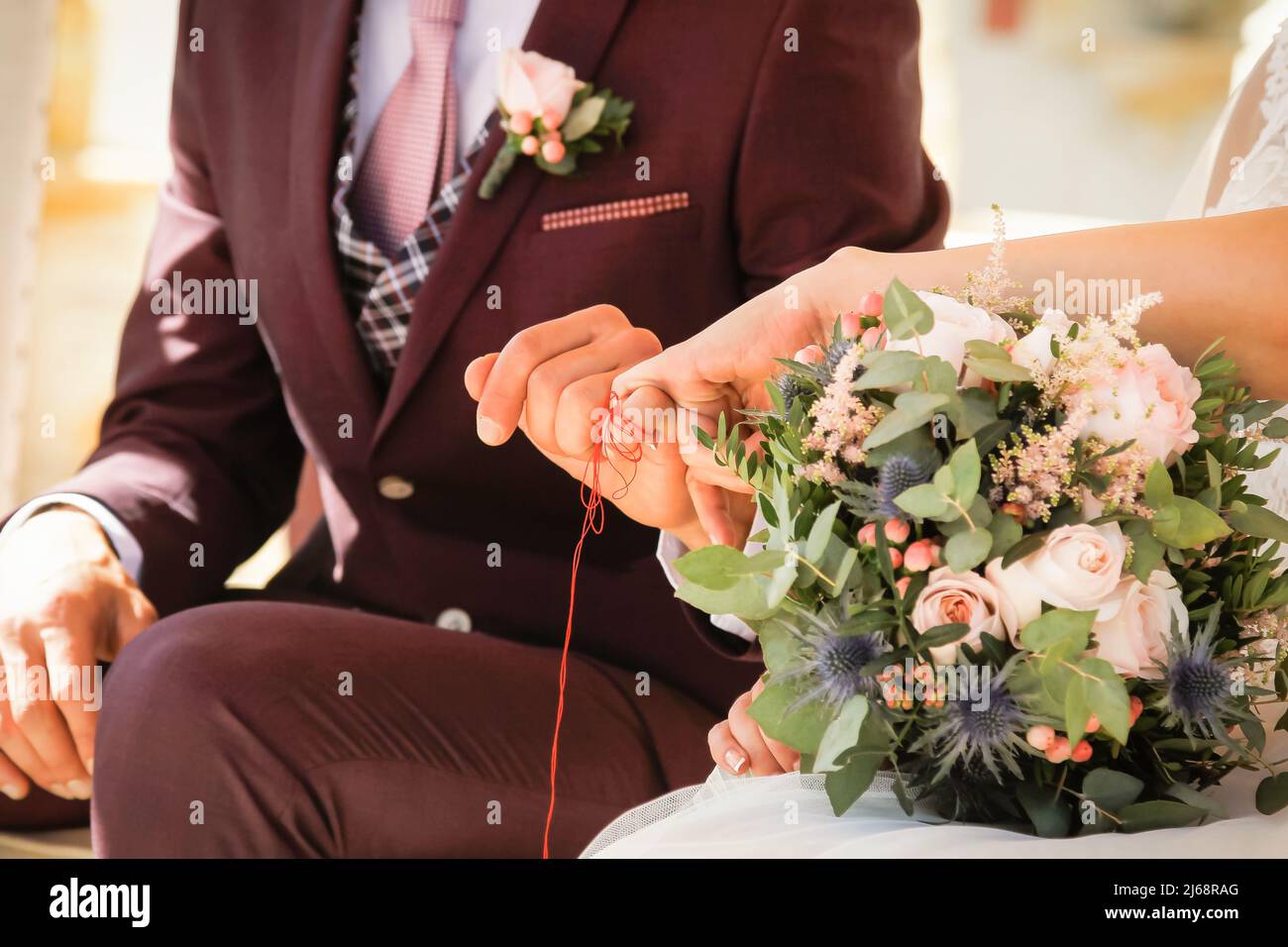 Filo rosso che unisce le dita della sposa e lo sposo nella celebrazione del loro matrimonio. Foto Stock