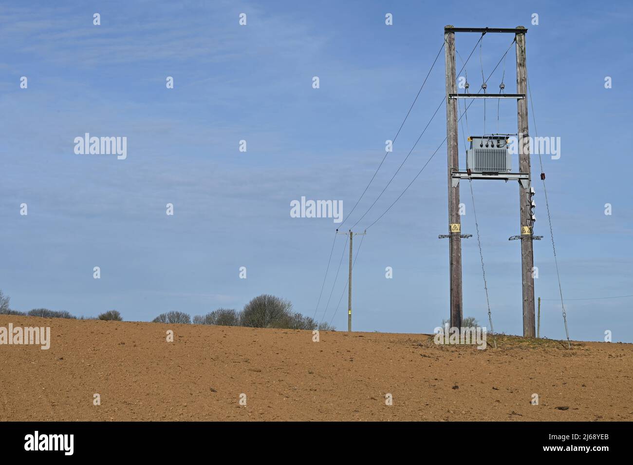 Piloni elettrici che attraversano un campo arato vicino al nord Oxfordshire villaggio di Hook Norton Foto Stock