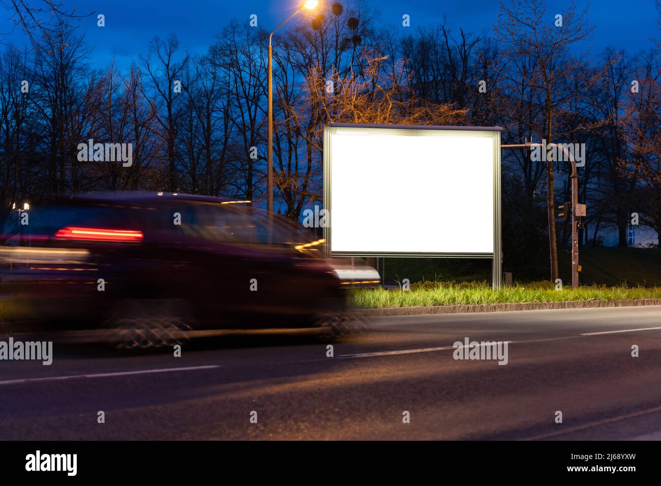 Pannello pubblicitario per affissioni per un mockup. Modello vuoto per un annuncio accanto a una strada con auto in movimento di notte. Spazio per la copia di un poster commerciale. Foto Stock