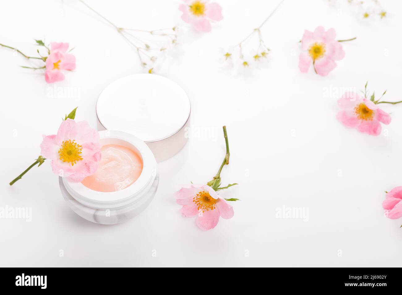 Contenitore cosmetico per fiori di crema e rosa rosato su sfondo bianco dall'alto, rosa selvaggia in cosmetici Foto Stock