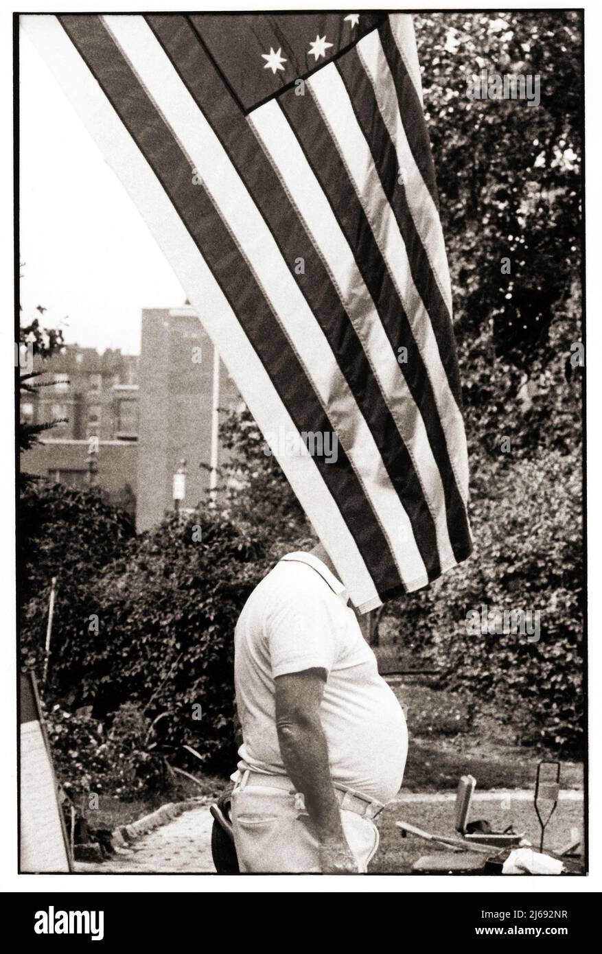 IL BRUTTO AMERICANO. Il ventre di vaso dell'uomo non identificato sporge da dietro una bandiera americana. A Brooklyn, New York circa 1973. Foto Stock