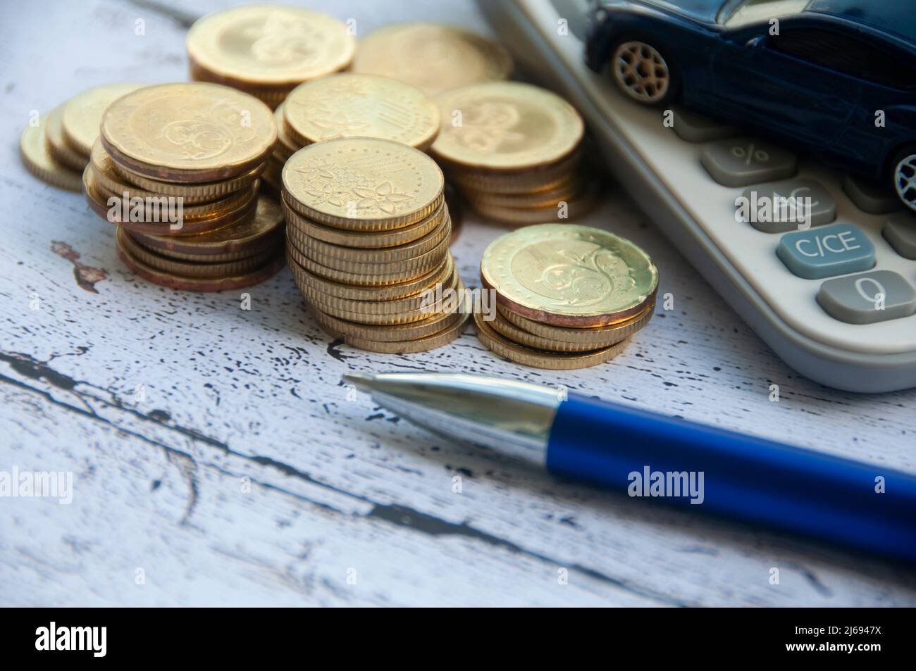 Monete d'oro, calcolatrice, giocattolo blu per auto e penna su sfondo di legno. Fuoco selettivo sulle monete. Finanza e copy space Foto Stock