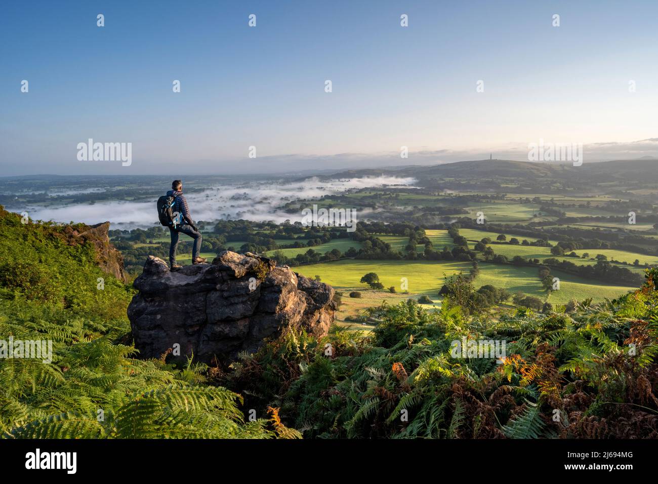 Un escursionista si trovava su una roccia a Cloudside guardando attraverso le pianure di Cheshire, Congleton, Cheshire, Inghilterra, Regno Unito, Europa Foto Stock