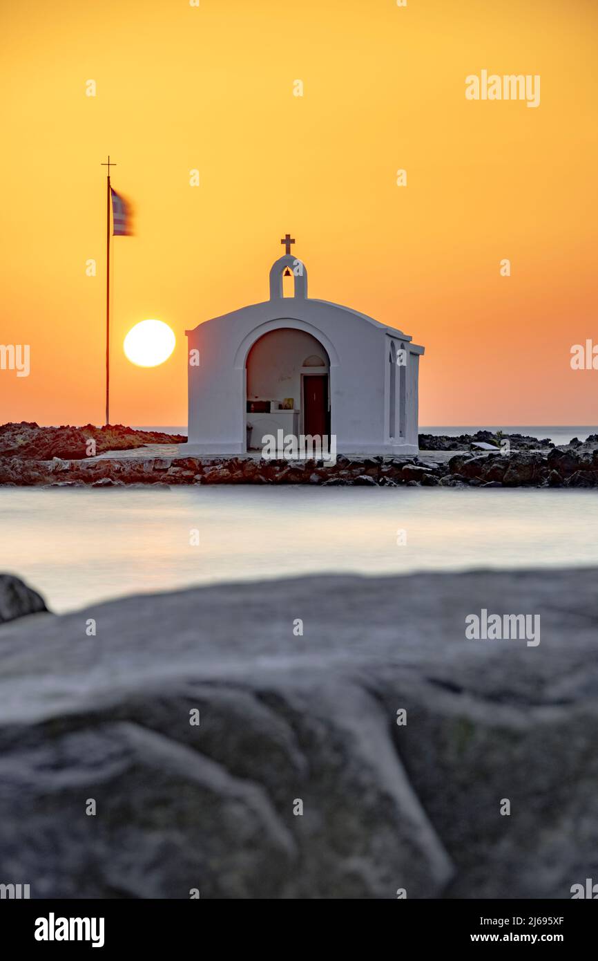 Sole che sorge sopra l'iconica chiesa di Agios Nikolaos e scogliere, Georgioupolis, isola di Creta, Isole Greche, Grecia Foto Stock