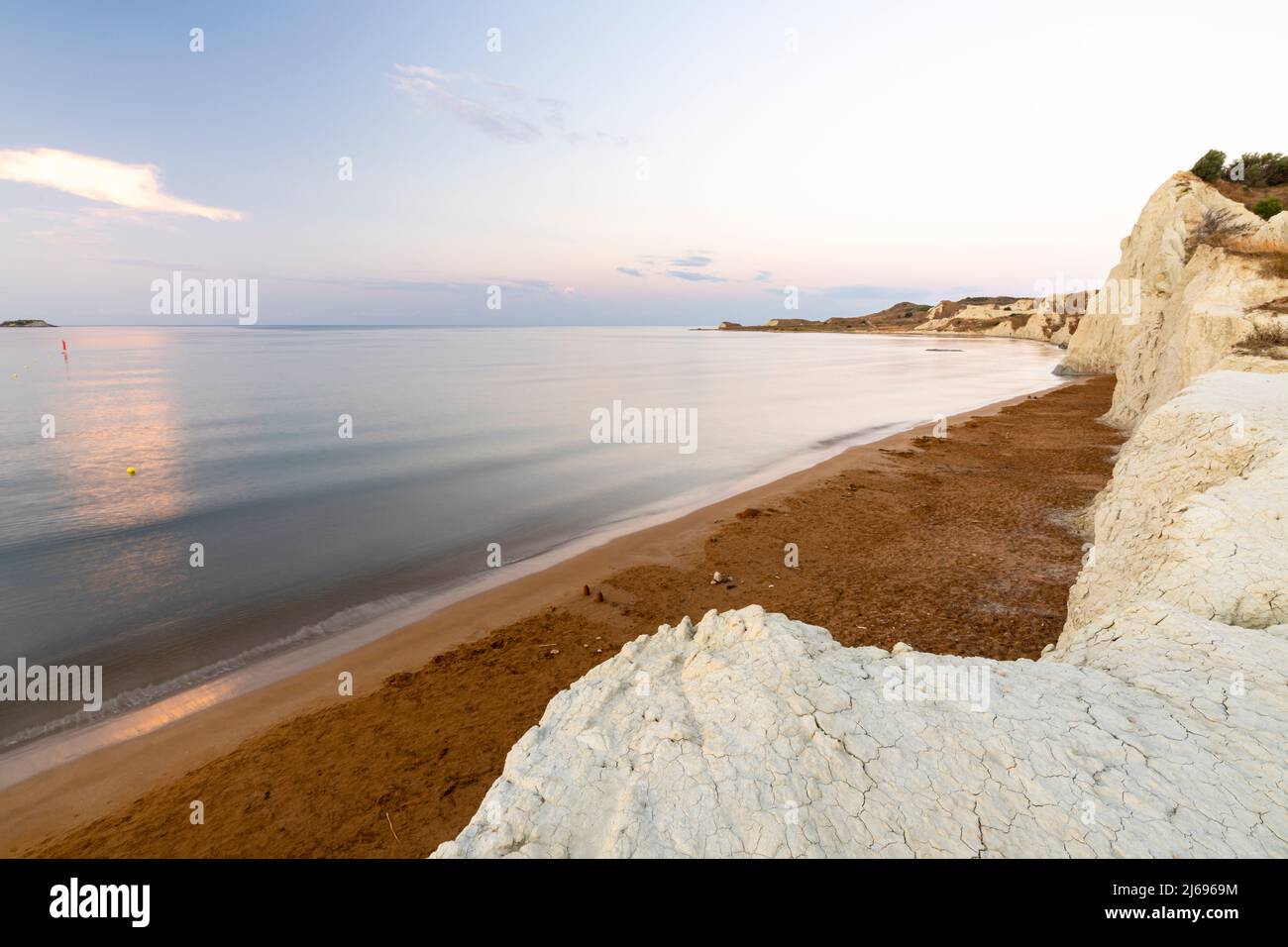 Mare calmo all'alba incorniciato da scogliere calcaree che si affacciano sulla sabbia dorata della spiaggia di Xi, Cefalonia, Isole IONIE, Isole Greche, Grecia, Europa Foto Stock