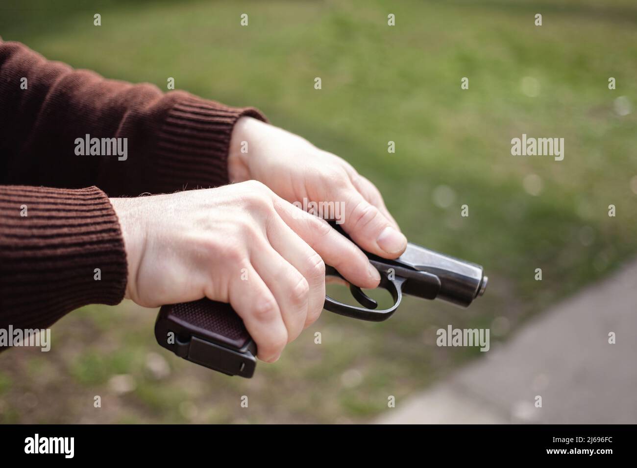 Un giovane uomo carica una pistola contro un'erba verde. Arma da fuoco all'aperto. Sport, hobby Foto Stock