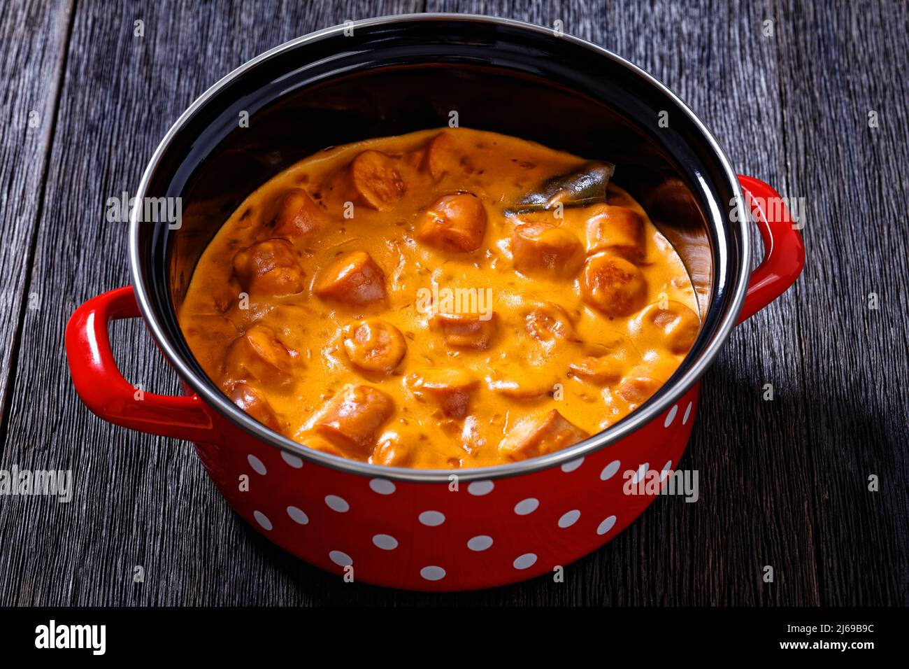 nakkikastike, salsicce finlandesi, amalgami in salsa di pomodoro cremosa in pentola rossa su tavola di legno scuro, vista orizzontale dall'alto, primo piano Foto Stock