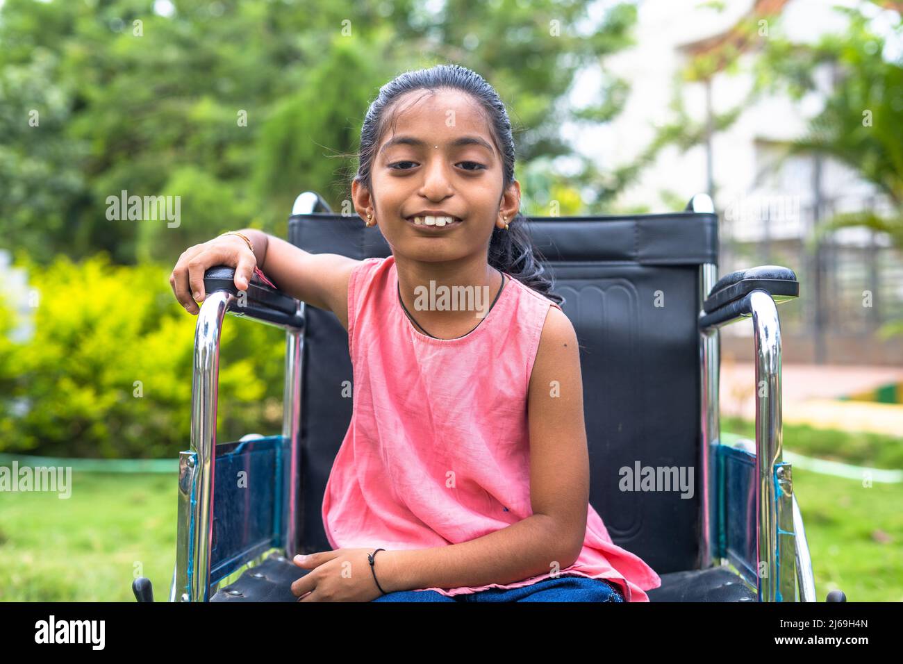 Concetto di recupero e ottimismo mostrando con felice sorridente bambino con disabilità su sedia a rotelle guardando con sicurezza la telecamera al parco. Foto Stock
