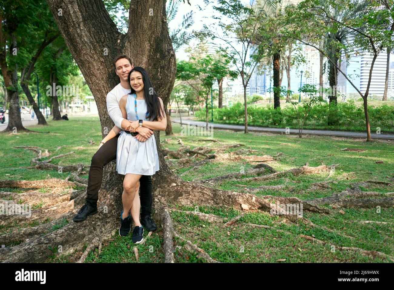 Foto con spazio di copia di una coppia multiculturale sposata di recente appoggiata su un albero Foto Stock