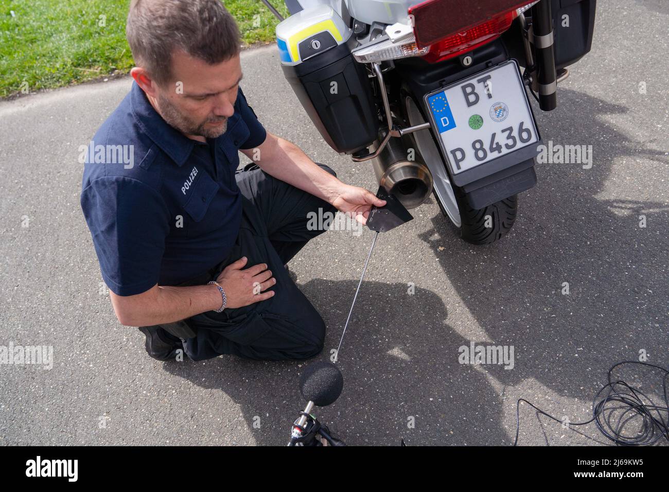 Baviera, Germania. 29th Apr 2022. 29 aprile 2022, Baviera, Aufseß: Un poliziotto dimostra come eseguire una misurazione del livello sonoro accanto a una motocicletta di servizio della polizia. Il ministro degli interni della Baviera Herrmann e l'ADAC Nordbayern hanno presentato misure per ridurre il rumore del traffico. Foto: Nicolas Armer/dpa Credit: dpa Picture Alliance/Alamy Live News Foto Stock