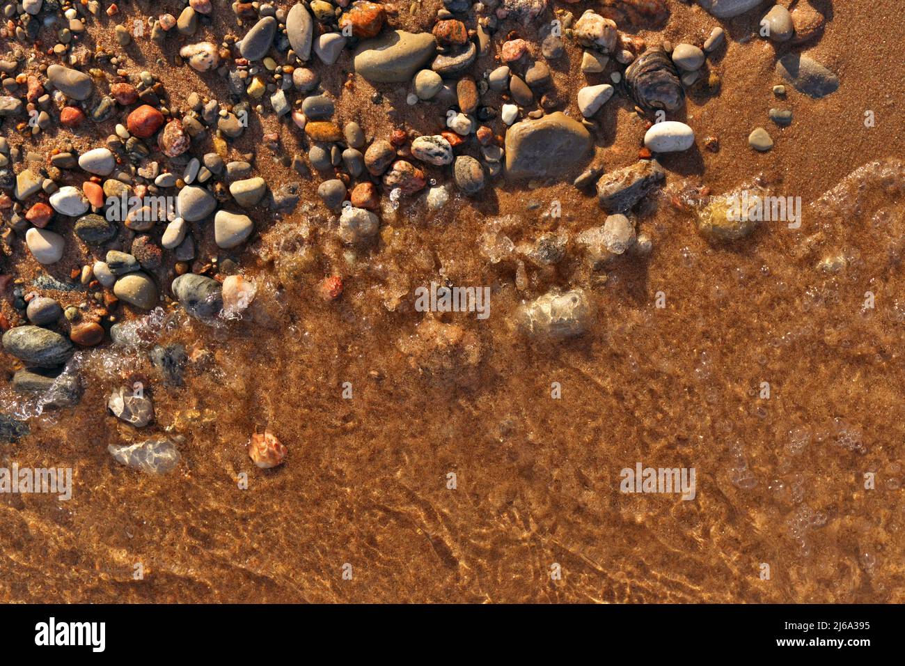 Direttamente sopra Flatlay di onde dolci che lambiscono sabbia e Pebble Beach con l'acqua pulita fredda incontaminata Foto Stock