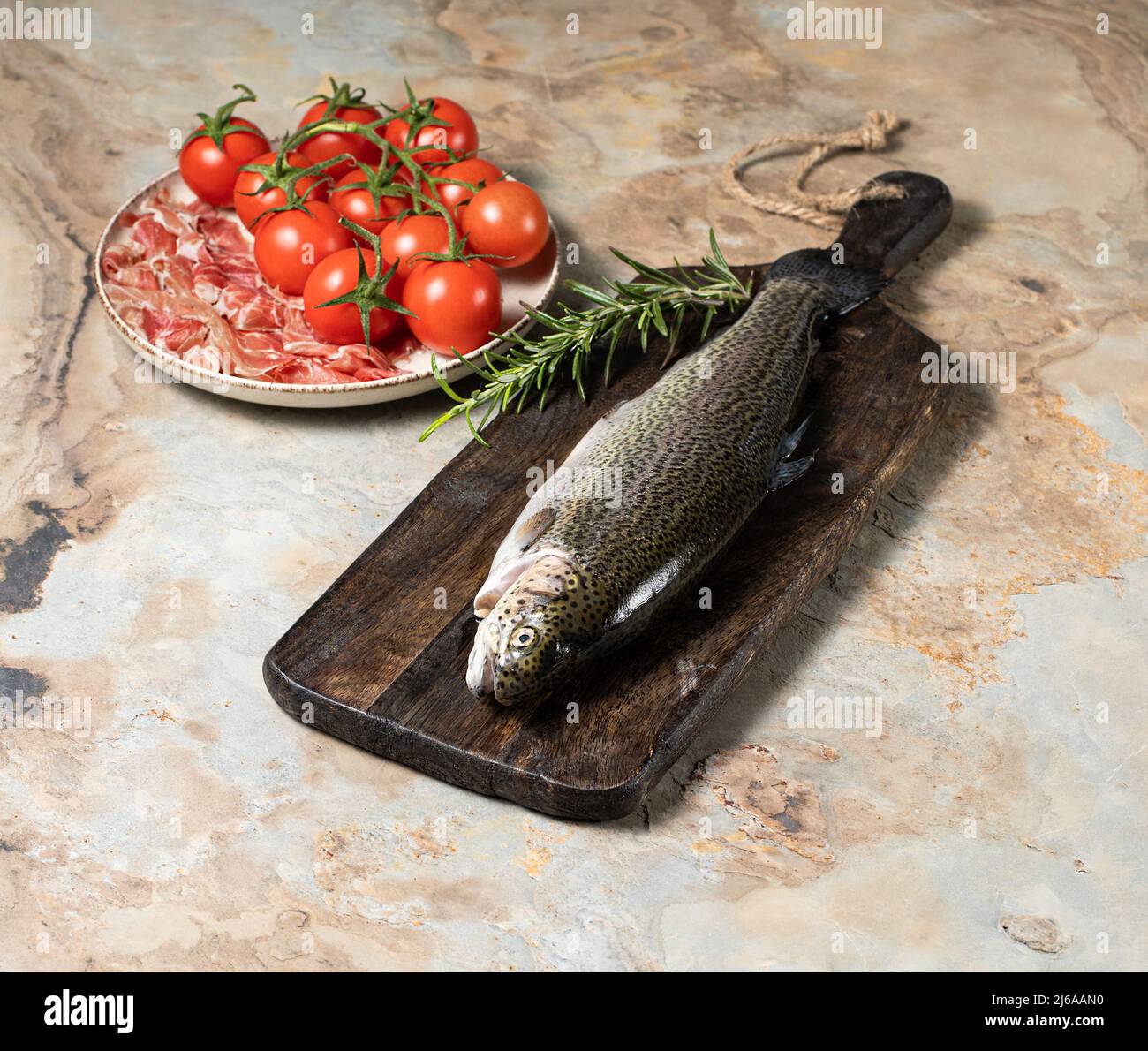 Trota cruda con rosmarino, prosciutto di parma e pomodori su sfondo ligneo vintage, sano concetto di mangiare, pesce. Foto di scorta Foto Stock