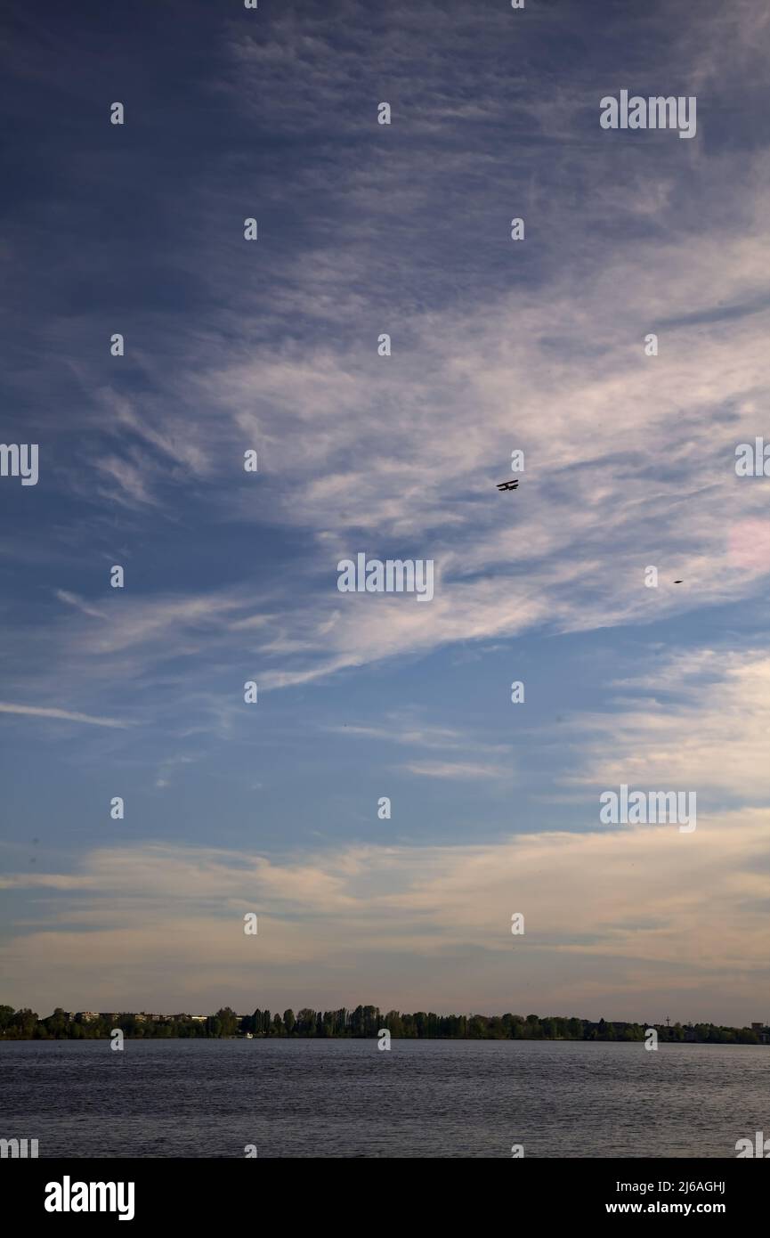 Lago al tramonto con la riva opposta in lontananza e un biplano nel cielo Foto Stock