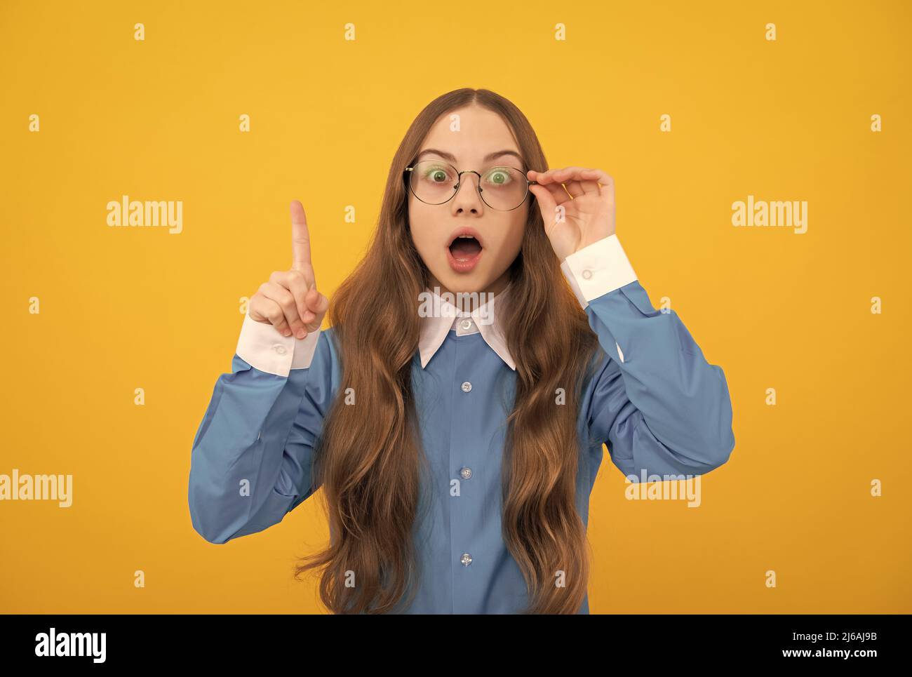Scioccata ragazza adolescente in occhiali ha avuto genio idea mantenere sollevato dito giallo sfondo, intelligente Foto Stock