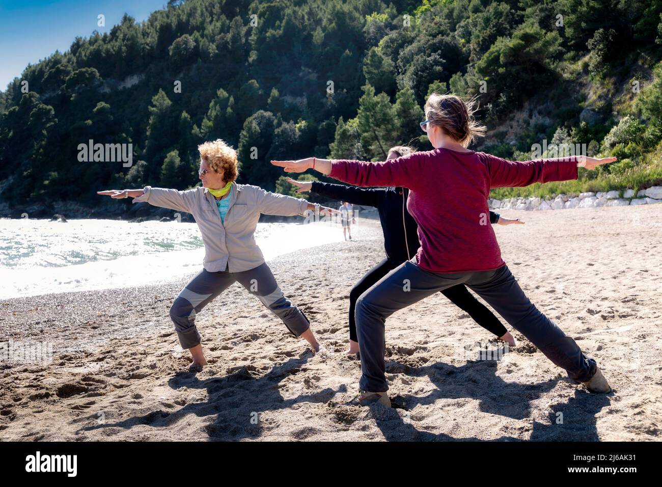 Tre donne fanno esercizi di yoga su una spiaggia vicino al mare. Foto Stock