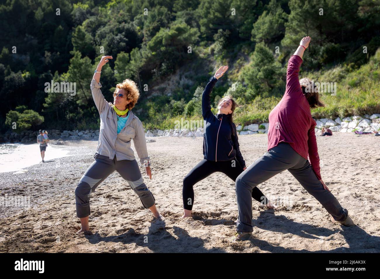 Tre donne fanno esercizi di yoga su una spiaggia vicino al mare. Foto Stock