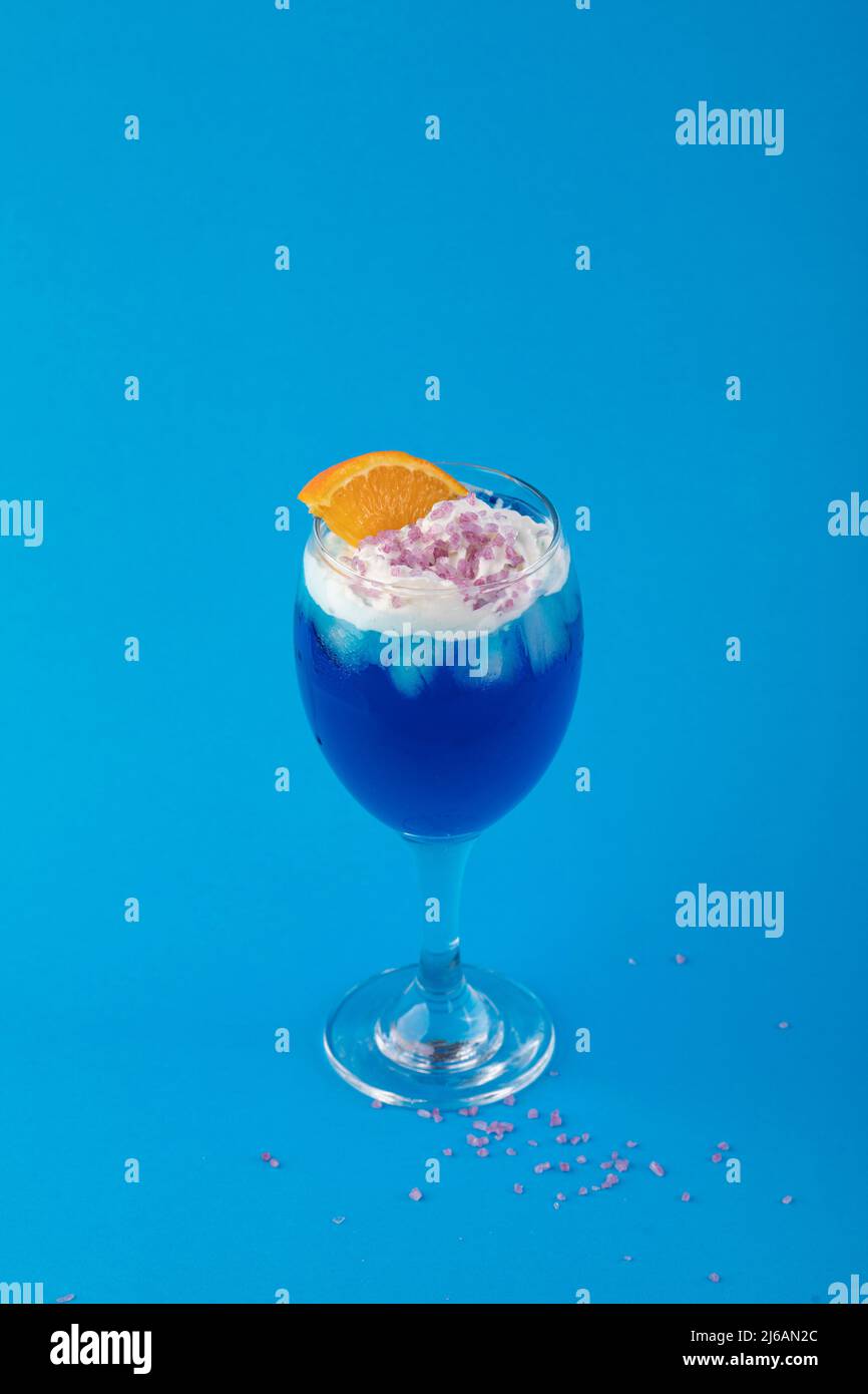 Cocktail blu con ghiaccio, fetta di arancia e panna montata Foto Stock