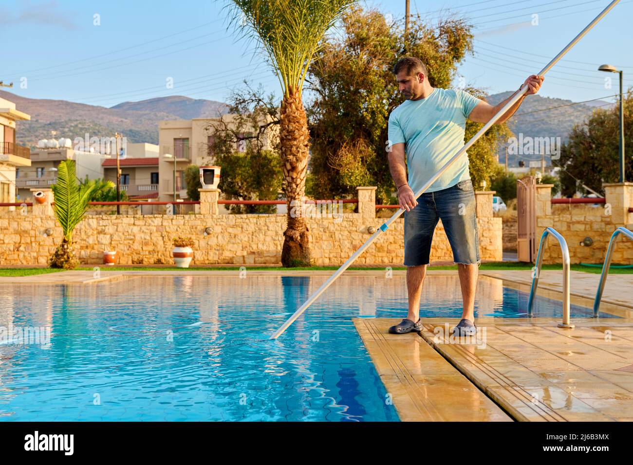 Uomo pulizia piscina esterna, bella vista panoramica della natura sfondo Foto Stock